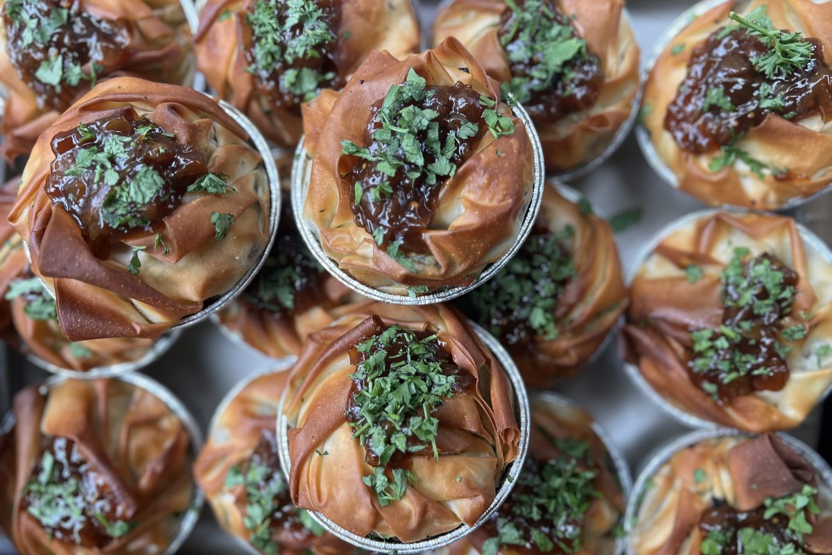 A close-up view of multiple filo pastry pies with golden, crispy layers, topped with a dark glaze and sprinkled with chopped fresh herbs.