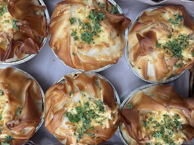 A tray of golden filo pastry pies with crisp edges and sprinkled with chopped herbs.