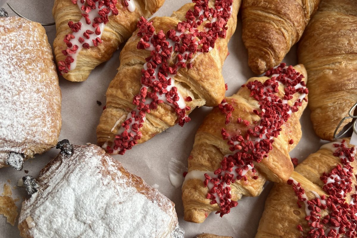 An assortment of pastries including croissants topped with icing and dried raspberry pieces, alongside pastries dusted with powdered sugar.