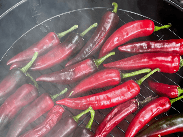 Red chillies grilling on a barbecue, surrounded by light smoke.