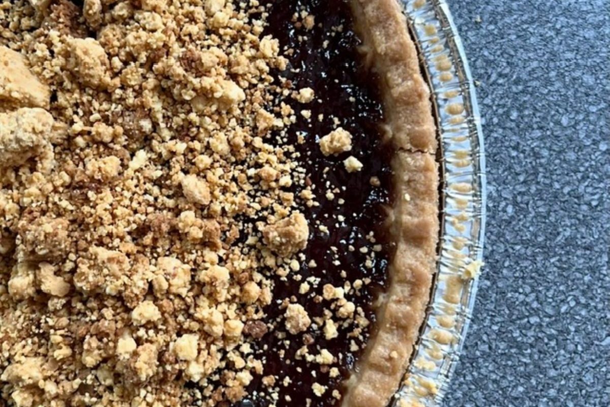 Handmade fruit crumble pie with a golden crumb topping and rich dark fruit filling in a foil baking dish.