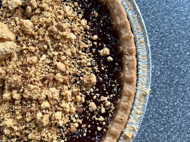 Handmade fruit crumble pie with a golden crumb topping and rich dark fruit filling in a foil baking dish.