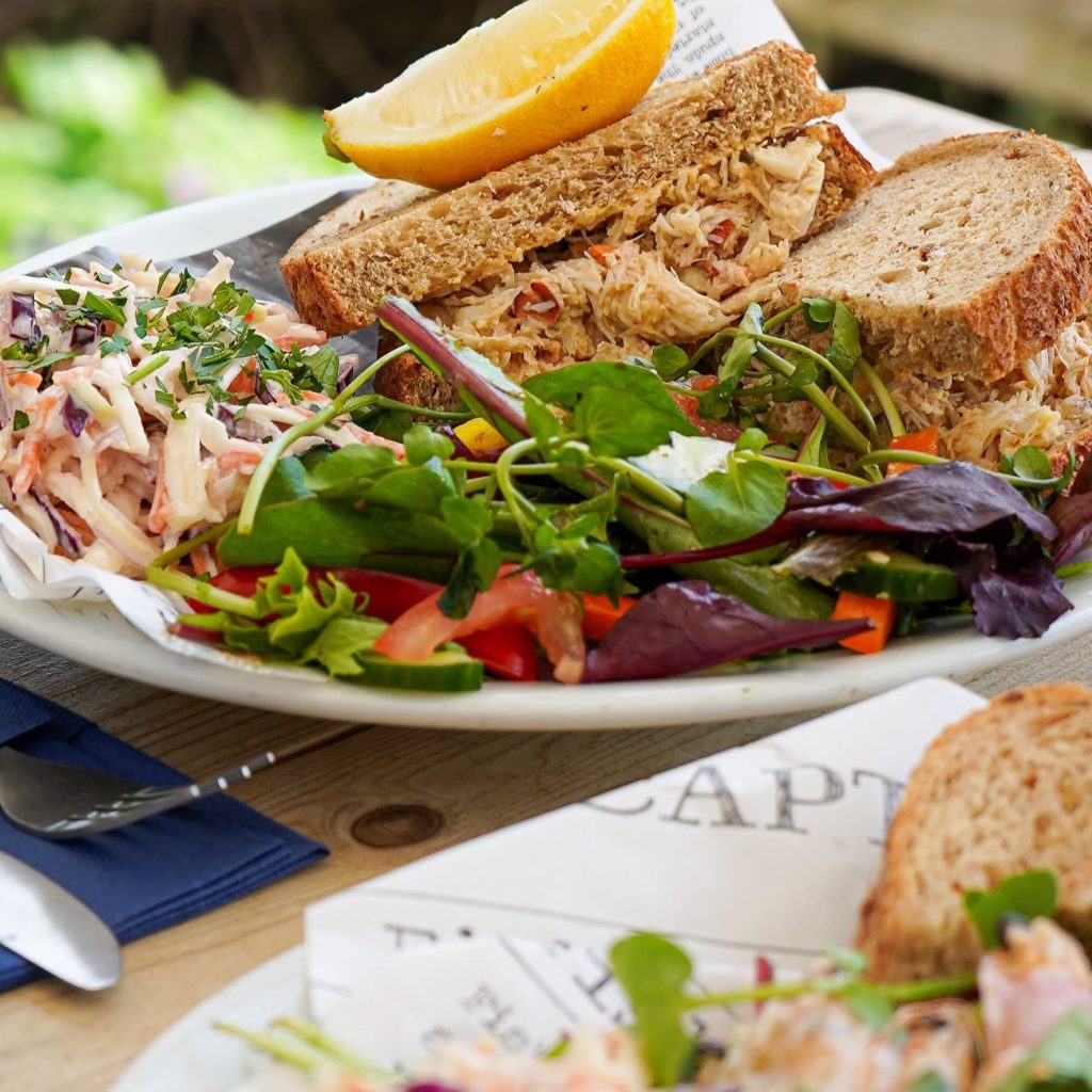 Crab sandwich with salad and coleslaw served outdoors at Hive Beach Café.
