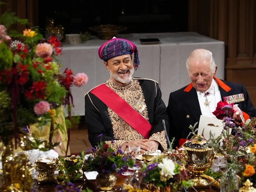 Guests seated at an elaborately decorated banquet table during a formal royal state banquet, surrounded by colourful floral displays, ornate gold tableware and candlelit centrepieces. The image captures part of the prestigious dining setting at Windsor Castle, where distinguished guests gathered for an official state occasion hosted by King Charles III.